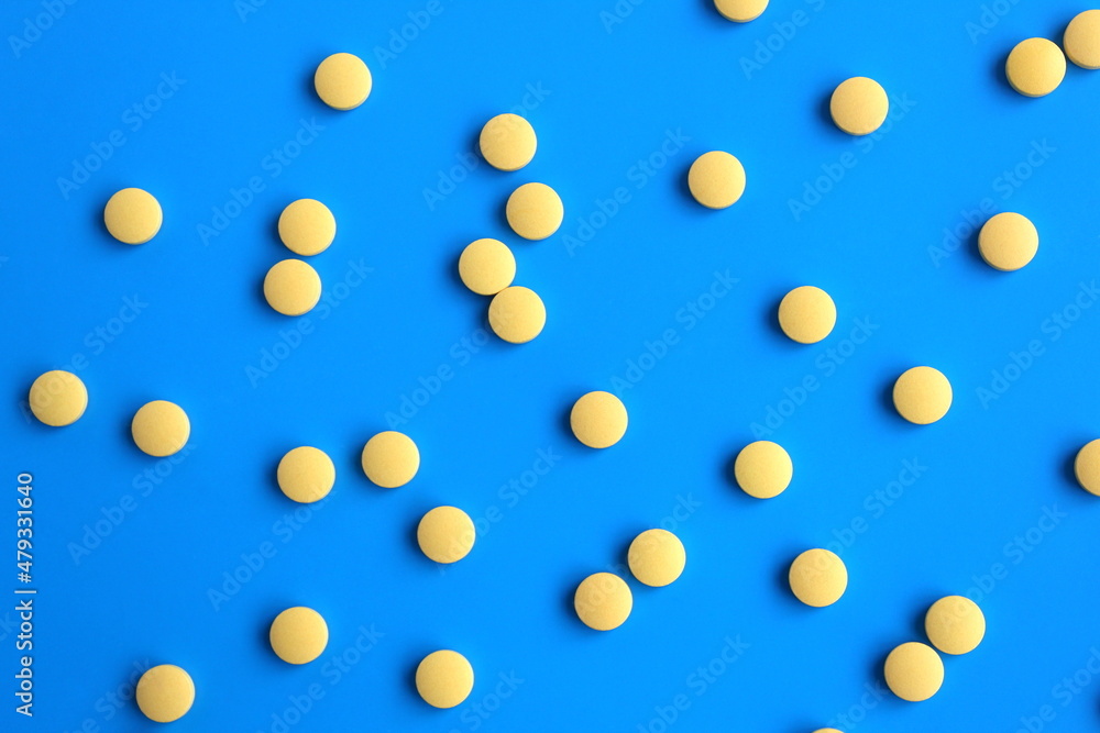 The texture of many yellow pills lie on a white background. The texture of many yellow pills lie on a white background.