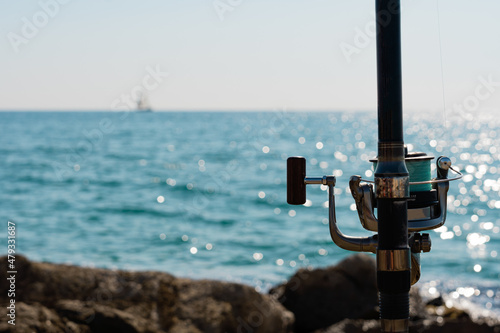 Close-up of fishing rod with sea and sailboat in the background, selective focus.