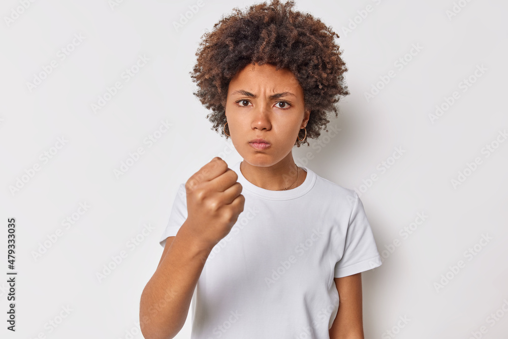 Angry outraged woman clenches fist with hatred expression warns about something irritated to lose competition grimaces with evil hateful face hates unfair results wears casual t shirt poses indoor Angry outraged woman clenches fist with hatred expression warns about something irritated to lose competition grimaces with evil hateful face hates unfair results wears casual t shirt poses indoor
