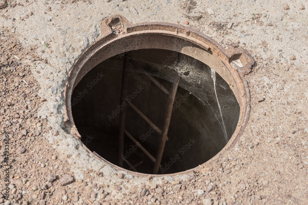 An open manhole on the road. Dangerous open unsecured hatch on the road. Accident with sewer hatch in city. Concept of sewage, repair of underground communications An open manhole on the road. Dangerous open unsecured hatch on the road. Accident with sewer hatch in city. Concept of sewage, repair of underground communications