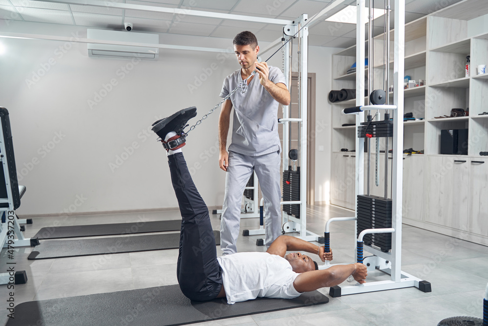 Fototapeta premium Man doing stretching exercise using gym equipment