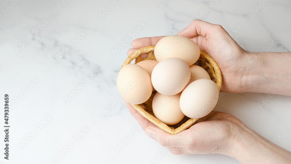 Woman holds a straw basket in her palms with large chicken eggs in her palms. Farm chicken eggs. Diet fresh produce. Space for text on the left, template for design, web banner Woman holds a straw basket in her palms with large chicken eggs in her palms. Farm chicken eggs. Diet fresh produce. Space for text on the left, template for design, web banner