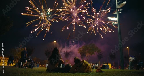 Unrecognizable family watch firework performance in the park, friends during light sky show during celebrations or festivities in the city. Big performance for national day or bank holiday