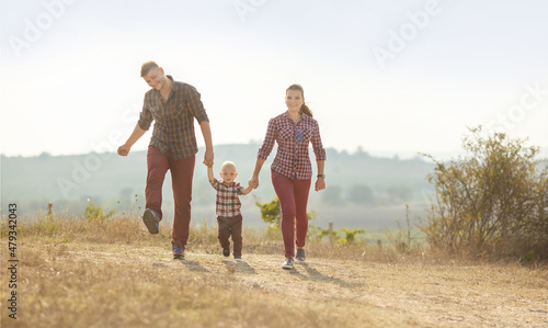 a young woman , a man and a little boy are having fun holding hands in a vineyard . They are dressed in plaid shirts