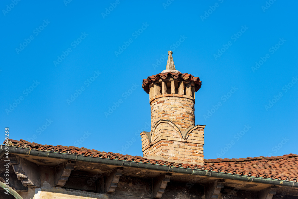 Close-up of an ancient chimney made of a bricks on a clear blue sky, on top of a roof with terracotta tiles (Coppo in Italian language). Vicenza downtown, Veneto, Italy, Europe.