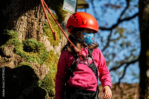 Little girl with protections practicing climbing between trees with ropes and nets