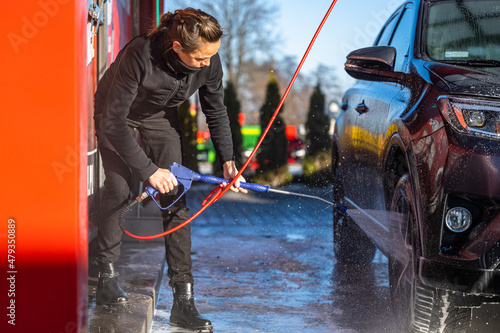 Young woman washing a car in a self-service car wash.