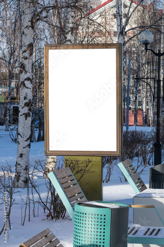 Billboard on the street in the city with an empty white space for text on a background of trees in frost, snow, blue sky, beautiful winter background, mockup