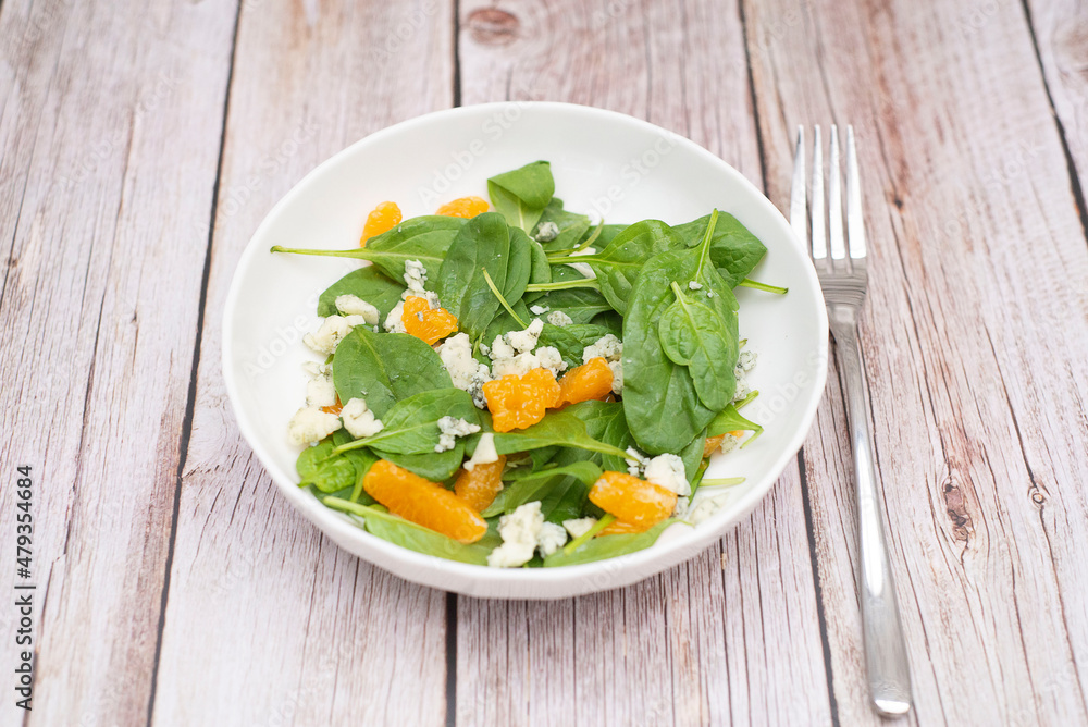 Healthy and light salad of spinach, tangerines and gorgonzola in white plate for snack. Healthy food. Diet food. Wooden background.