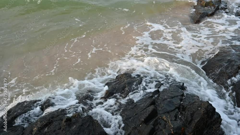 ocean wave splashes across a big rock in the middle of the rough exotic sea breaking wave foaming over a black rock near rocky tropical shore. ocean wave splashes across a big rock in the middle of the rough exotic sea breaking wave foaming over a black rock near rocky tropical shore.