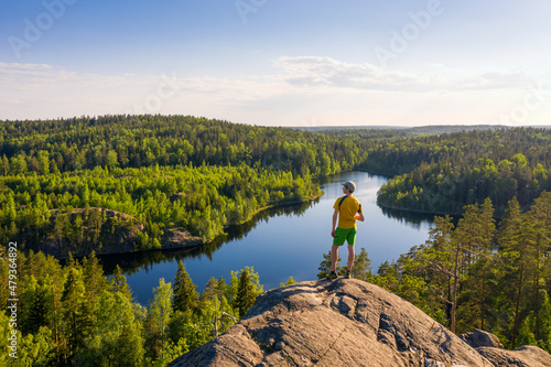Summer landscape with a man contemplating the beauty of nature on a hill against the backdrop of a lake.