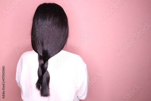 Dark female braided hair.A woman in a white shirt stands with her back on a light background. 