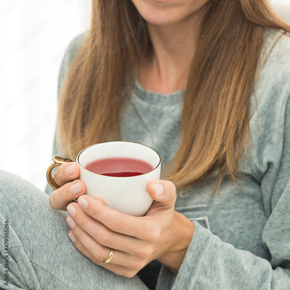 Mulher com roupa cinza e branca tomando xícara de chá vermelho com notebook cinza Mulher com roupa cinza e branca tomando xícara de chá vermelho com notebook cinza