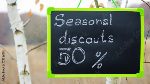 frame with text. seasonal, autumn discounts. Chalkboard and autumn leaves. natural background. the sign with the text weighs on the tree. sale, big discounts, 50 percent. trade and business concepts