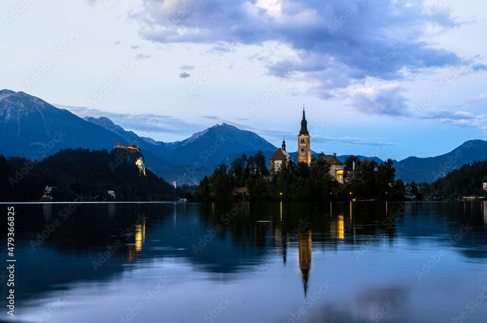 Evening sunset at Lake Bled in Slovenia. Enlightened church on the island, castle ba rock and mountains in the setting sun.