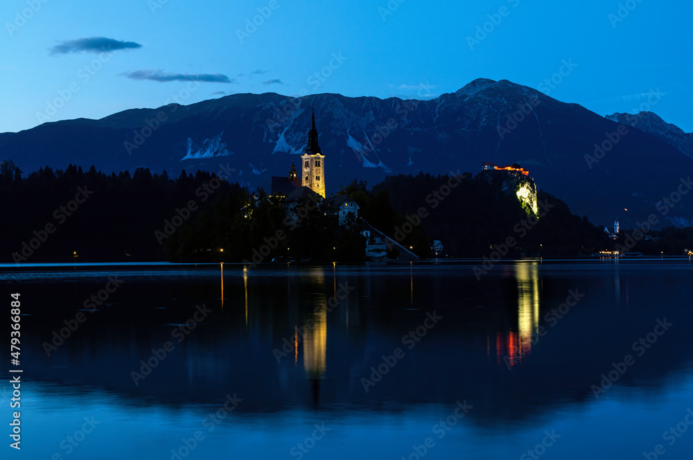 Evening sunset at Lake Bled in Slovenia. Enlightened church on the island, castle ba rock and mountains in the setting sun.