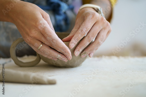 Art therapy for mental health. Closeup of female ceramics master create craft cup of wet pot. Table of pottery workshop owner with material for shaping handicraft tableware. Artist at work in studio