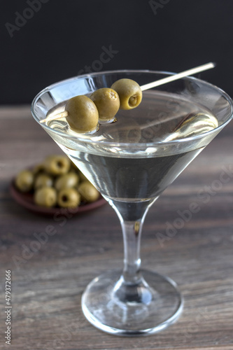 Martini cocktail in a triangular glass with green olives on a dark wooden background.