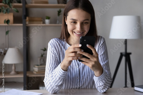 Happy girl using smartphone  reading on screen  texting  smiling. Digital addicted woman chatting on social media  shopping online  making video call  playing virtual game at office workplace table