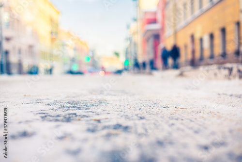 Winter in the city. Empty street. Snow cover. Pedestrians are walking. Sunny day. Focus on road. Close up view from the level of the road.