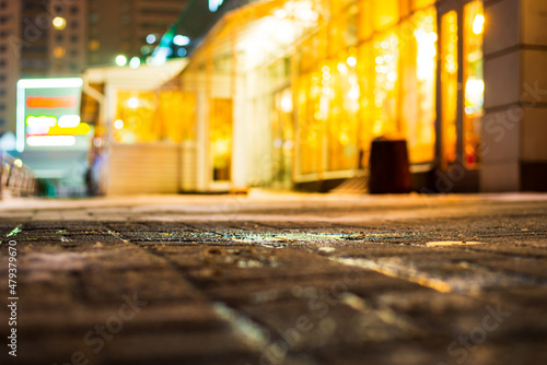 Winter in the night city. Illuminated showcase of a shopping center. Christmas decorations. Working lights. Juicy colors. Focus on the tiled sidewalk. Close up view from sidewalk level.