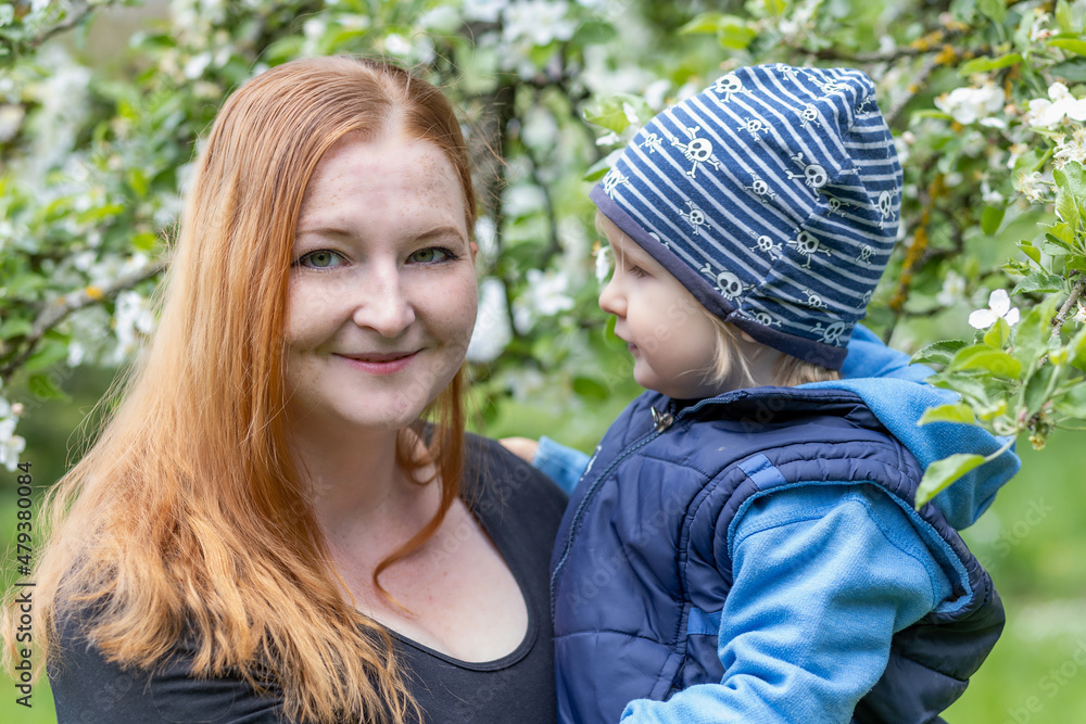 Portrait of young mother and her cute little son she is holding in her arms under a flowering tree. Portrait of young mother and her cute little son she is holding in her arms under a flowering tree.
