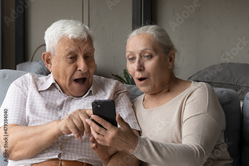 Happy surprised middle aged old 70s retired family couple looking at cellphone screen, feeling excited reading message with amazing unbelievable news, celebrating online lottery gambling auction win.