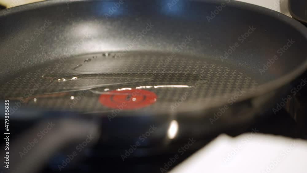 Cooking on electric stove top in the kitchen, woman sprinkles frying pan with vegetable oil on induction cooktop closeup. High quality 4k footage Cooking on electric stove top in the kitchen, woman sprinkles frying pan with vegetable oil on induction cooktop closeup. High quality 4k footage