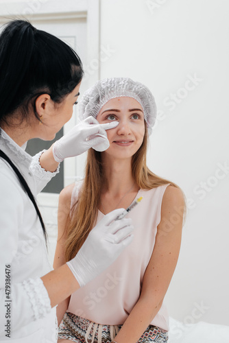 The cosmetologist wipes the patient's face after the procedure of filling the nasolacrimal furrow and mesotherapy around the eyes for a young beautiful girl. Modern cosmetology.