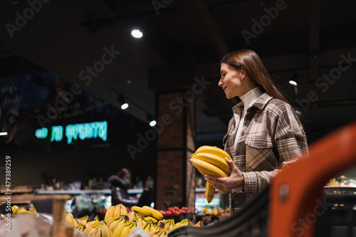 Girl buys bananas in the fruit section of the supermarket