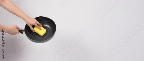 Cleaning Electric non stick pan. Hand on white background cleaning the non stick pan with handy dish washing sponge which yellow color on the soft side and green on hard side for hygiene after cook.