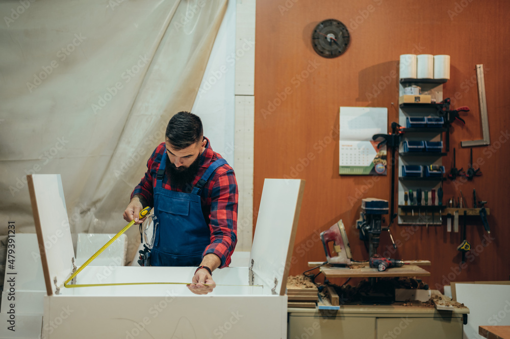 Young male carpenter working in workshop and measuring with meter Young male carpenter working in workshop and measuring with meter