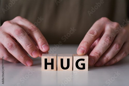 A businessman holds wooden cubes with the word hug.