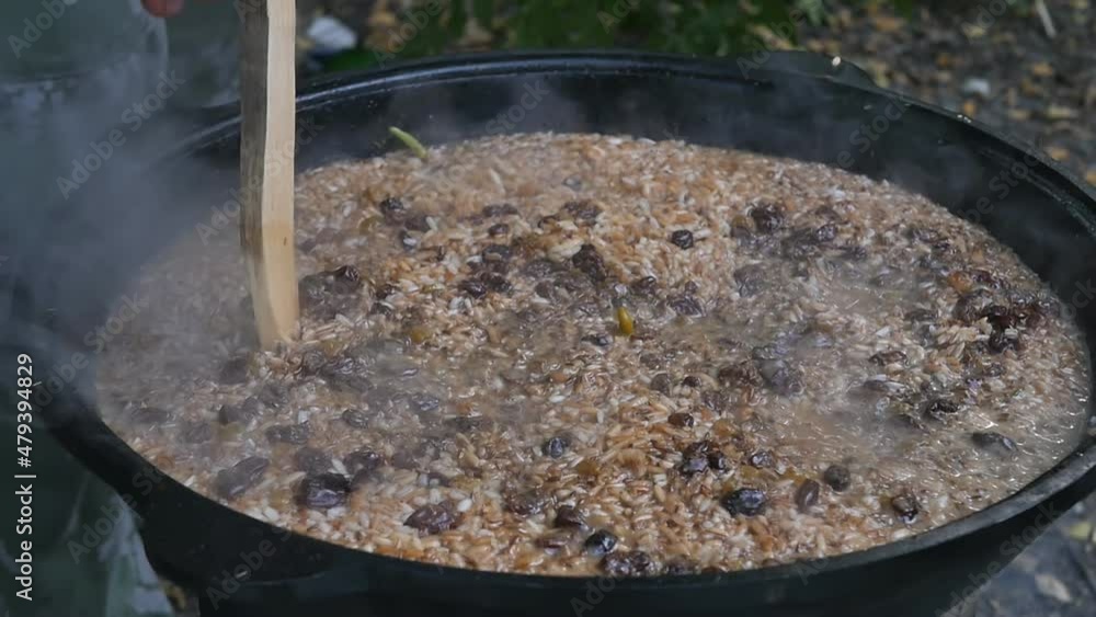 Uzbek man prepares national pilaf in a large cauldron in the open air. Pierces with a wooden stick for better penetration Uzbek man prepares national pilaf in a large cauldron in the open air. Pierces with a wooden stick for better penetration