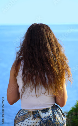 The back of a girl with long brown hair looking towards the sea horizon in front of her
