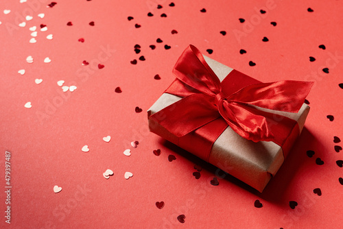 Red gift box with a ribbon for Valentines Day celebrating on red solid background with copy space