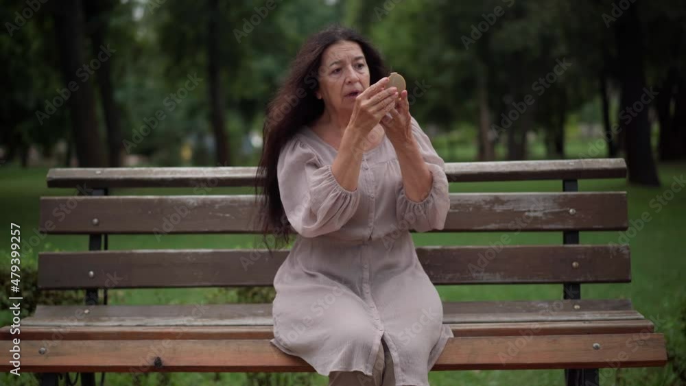 Front view wrinkled senior Caucasian woman looking in hand mirror sitting on bench in park sighing looking away. Worried sad retiree dislike reflection making stressed facial expression. Aging concept Front view wrinkled senior Caucasian woman looking in hand mirror sitting on bench in park sighing looking away. Worried sad retiree dislike reflection making stressed facial expression. Aging concept