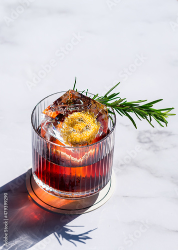 Fotografie alcoholic cocktail negroni with a block of ice on a light background with a shad