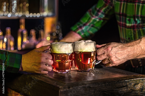 Male hands with mugs of beer, ale on the bar counter. Holiday of Ireland on St. Patrick's Day in irish pub, bar. National tradition of carnival celebrating March 17