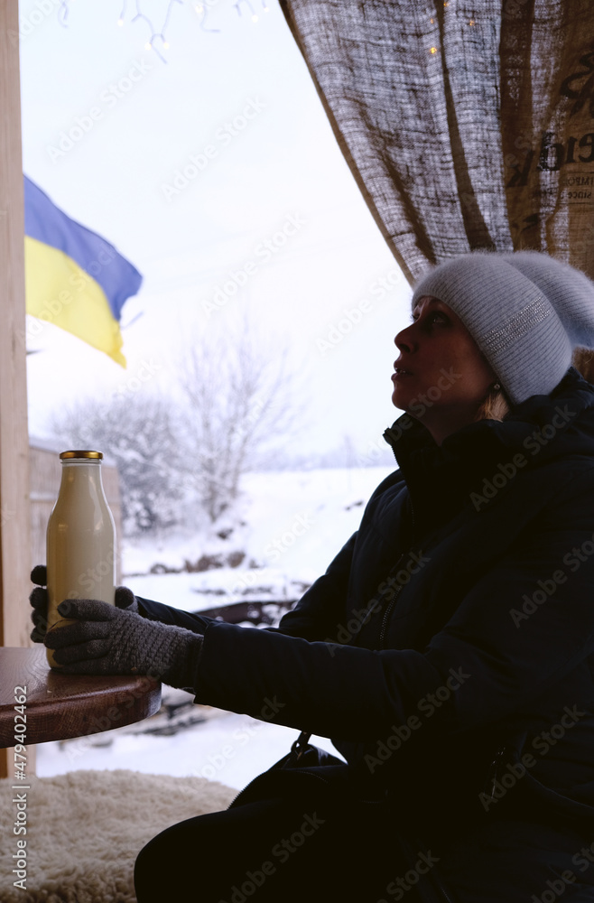 morning farm milk in a glass bottle in the hands of a girl in winter. Ukraine flag on background. Farming, eco products, eco-friendly packaging