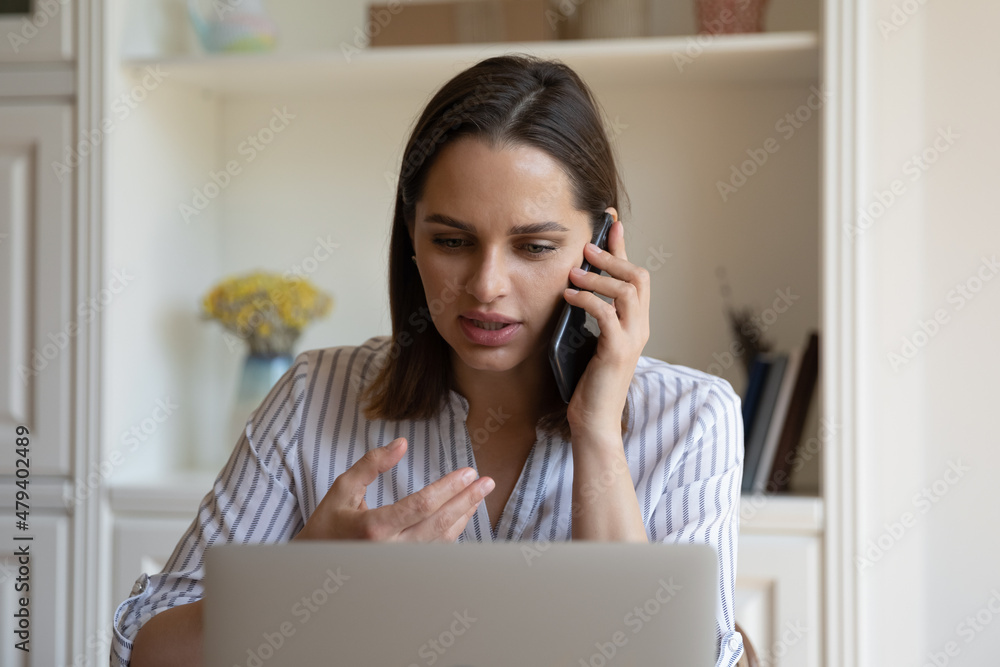 Focused millennial business professional woman talking to client on mobile phone, making telephone call from office workplace, negotiating on project, consulting work app on laptop computer Focused millennial business professional woman talking to client on mobile phone, making telephone call from office workplace, negotiating on project, consulting work app on laptop computer