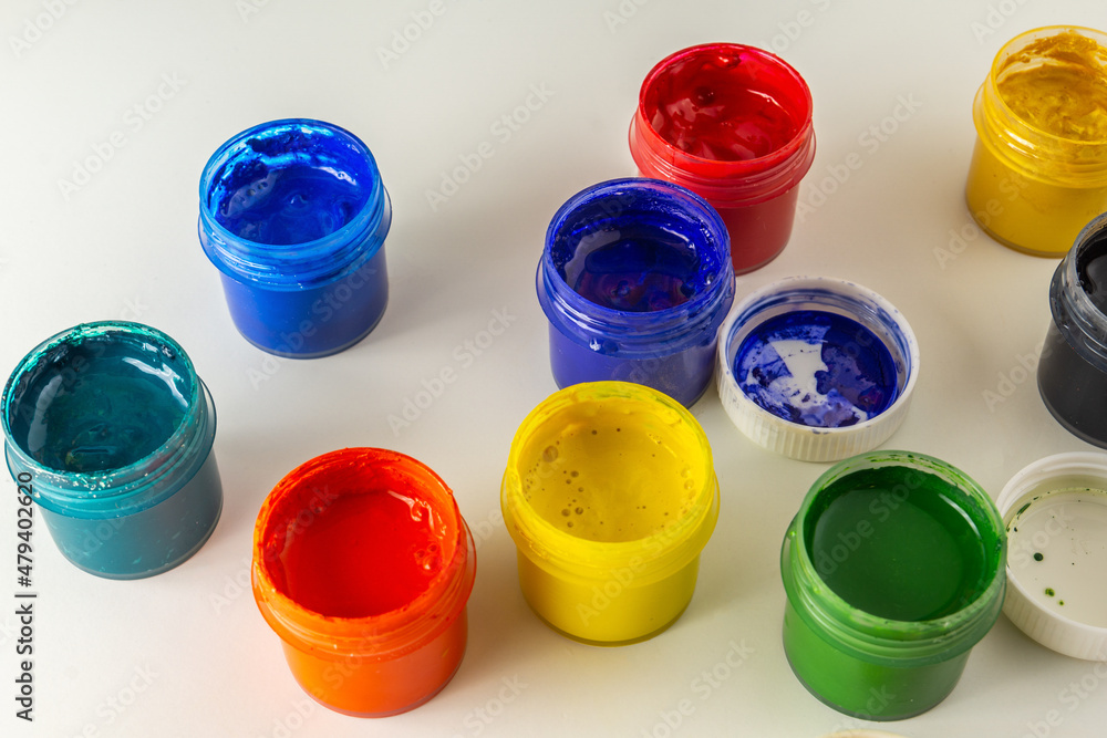 Opened jars of multi-colored gouache on a white background. Lids stained with paint, a creative mess. Drawing training. Top view Opened jars of multi-colored gouache on a white background. Lids stained with paint, a creative mess. Drawing training. Top view