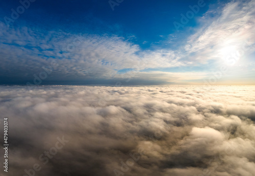 Aerial view of vibrant yellow sunrise over white dense clouds with blue sky overhead