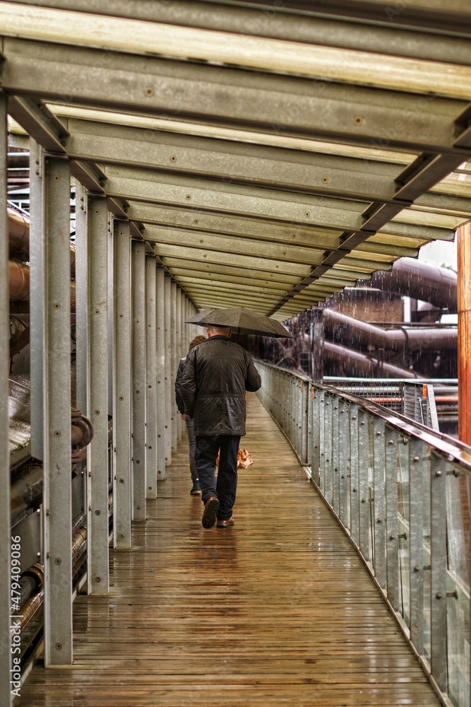 Hombre con paraguas en la lluvia en ambiente industrial