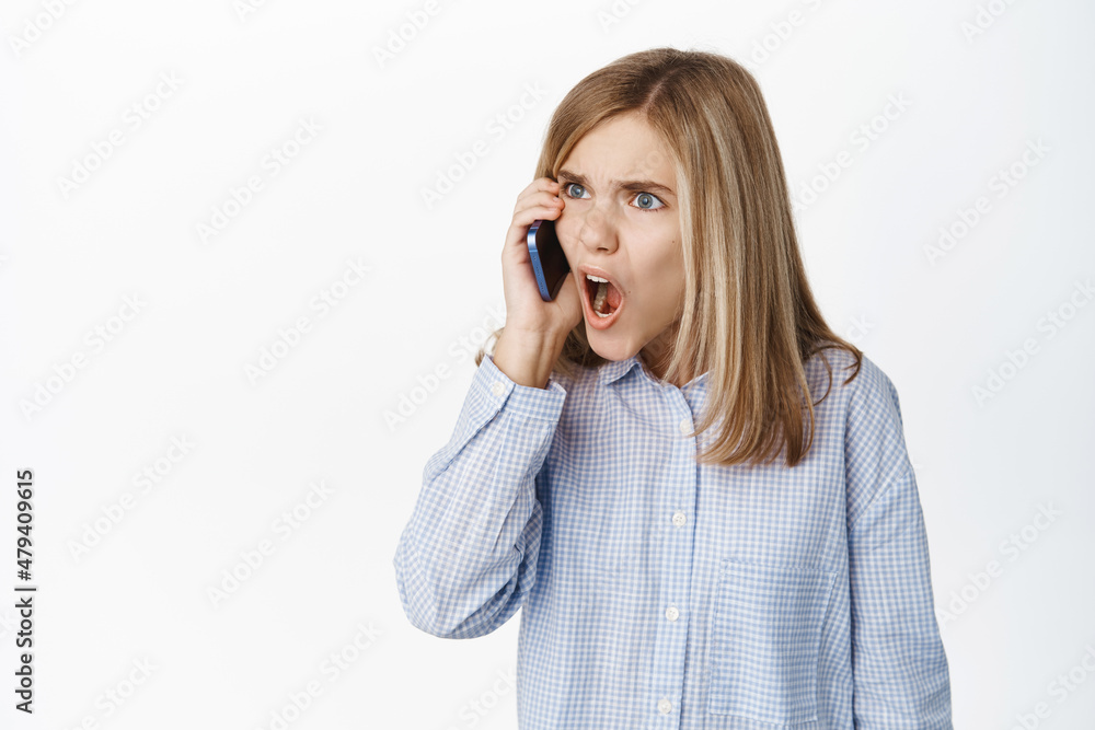Cute little girl, beautiful blond kid talking on mobile phone, having conversation on smartphone, answer a call, standing over white background Cute little girl, beautiful blond kid talking on mobile phone, having conversation on smartphone, answer a call, standing over white background