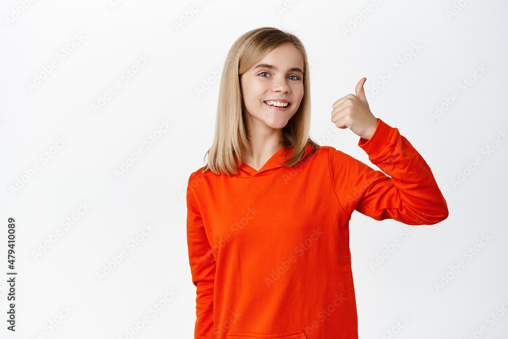 Cheerful blond little girl shows thumbs up in approval, smiling pleased and making compliment, satisfied by smth good, standing over white background Cheerful blond little girl shows thumbs up in approval, smiling pleased and making compliment, satisfied by smth good, standing over white background