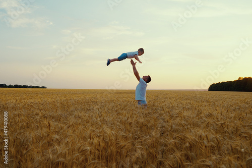 Father throwing little son up in the air in wheat field in slow motion. Parent and child having fun and enjoying time together. Concept of happiness