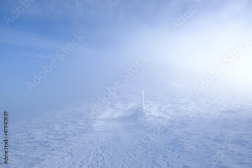 A frozen pole marking trail in the mountains by path on foggy and sunny winter day. Babia Gora peak in background. Diablak, Beskid Zywiecki, Poland