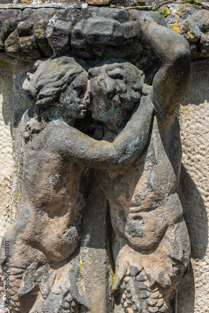 Two stone figures are kissing. Embracing male and female half figures carrying a ledge in a baroque garden