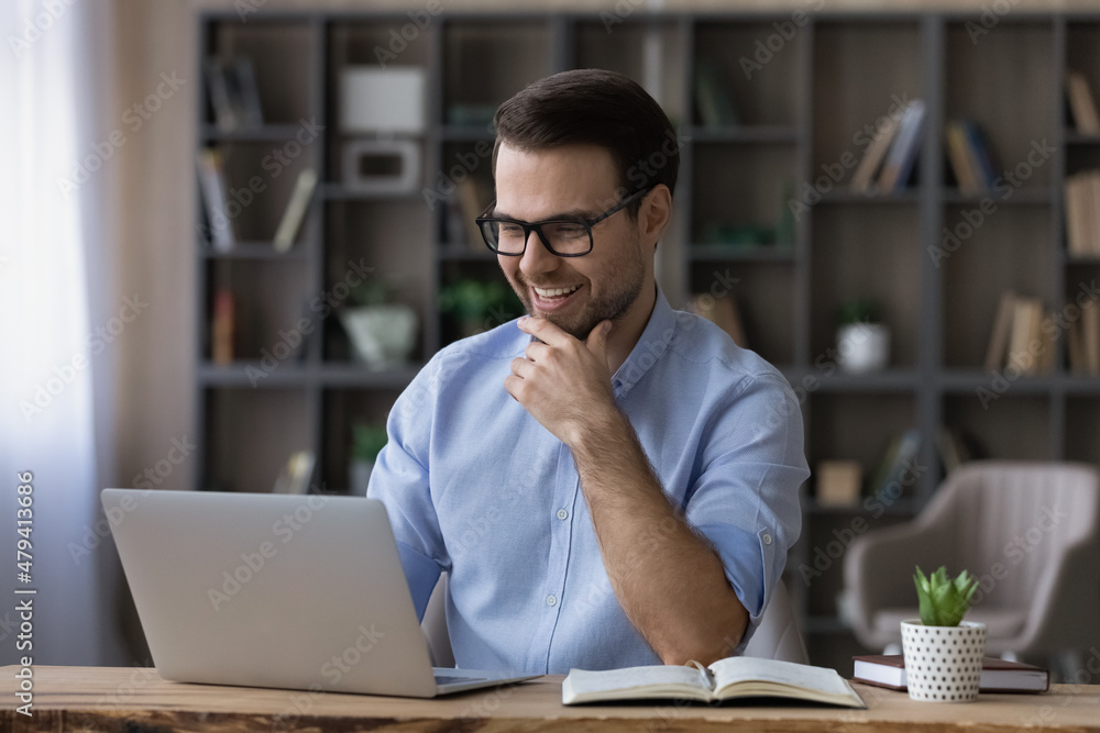 Excited successful businessman in glasses looking at laptop screen, reading good news in message or email, happy laughing young man freelancer or student received unexpected offer, notification